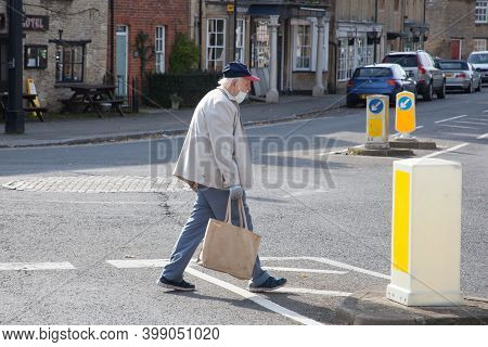 A Elderly Man Crosses A Road In Bampton, Oxfordshire Wearing A Face Mask In The Uk, Taken 19th Octob