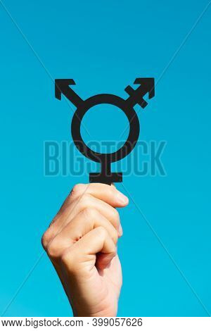 closeup of a young caucasian person showing a transgender symbol against the blue sky