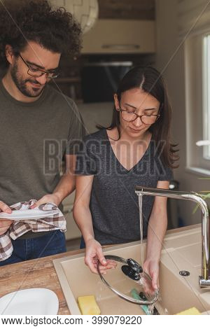 Beautiful Young Couple In Love Doing The Washing Up Together After Lunch; Woman Washing The Dishes W