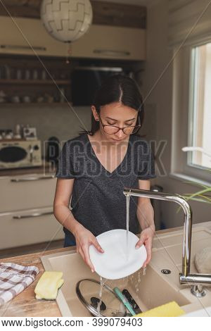 Young Woman Standing By The Kitchen Sink, Washing The Dishes After Lunch; Woman Doing The Washing Up
