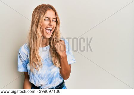 Beautiful blonde young woman wearing tye die tshirt celebrating surprised and amazed for success with arms raised and eyes closed 