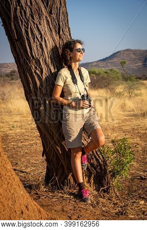 Brunette Stands Leaning Against Tree With Binoculars
