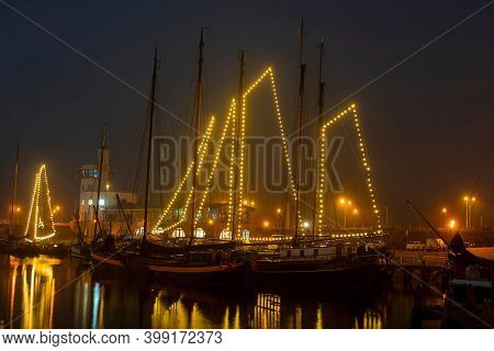 Decorated traditional sailing ships in the harbor from Harlingen in the Netherlands in christmastime at night