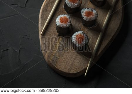 Classic Sushi With Salmon On A Wooden Board On A Stone Black Table. Nearby Are Chinese Sticks. Top V
