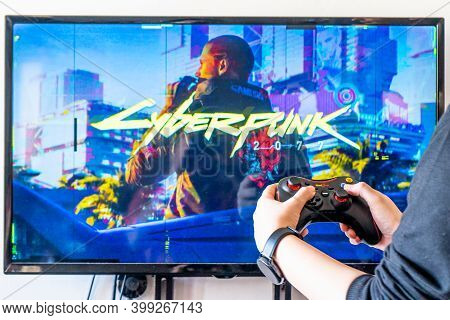 Woman Holding A Red Gear Controller And Playing Popular Video Game Cyberpunk 2077 On A Television An