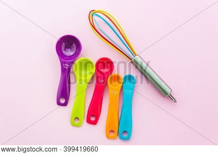 Collection of colorful measuring spoons and whisk use in cooking process on pink background