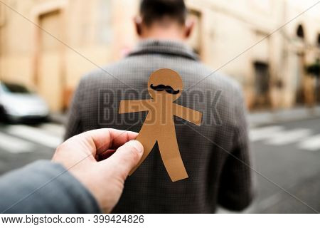a man is about to attach a paper man doll to the back of another man, as a prank for dia de los inocentes, the innocents day, a feast held in spain and hispanic america equivalent to april fools day