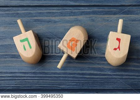 Hanukkah Traditional Dreidels With Letters He, Pe And Gimel On Blue Wooden Table, Flat Lay