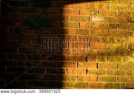 A Textured Brick Wall With Moss Growing On It And Half Lit By Orange Light Coming Through A Window