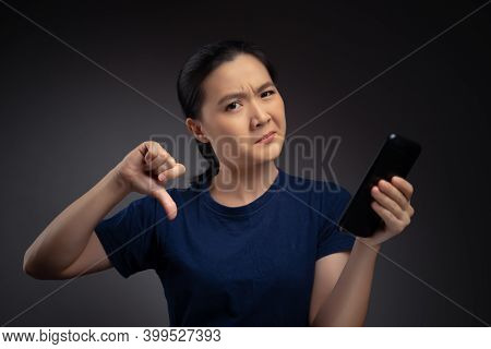 Asian Woman Looking At Smart Phone And Showing Thumb Down.