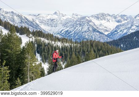 Senior Man Is Snowshoe Hiking In Alpine Snow Winter Mountains. Allgau, Bavaria, Germany.