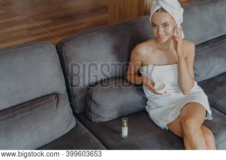 Top View Of Happy Caucasian Woman Satisfied With Healthy Smooth Perfect Skin, Applies Face Cream, Wr
