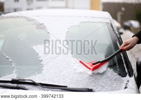 A Man Cleans Snow From The Windshield Of A Car With A Red Brush
