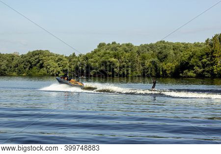 Speedboat Towing An Athlete On A Board Against The Background Of The Forest. Athlete Water Skiing An