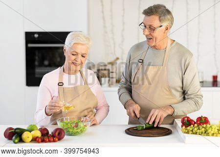 Senior Couple Enjoying Food Preparation Together Cooking Making Salad In Modern Kitchen Indoor. Matu