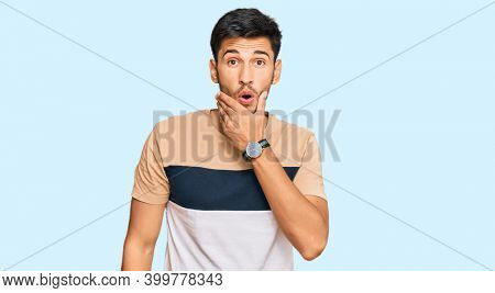 Young handsome man wearing casual clothes looking fascinated with disbelief, surprise and amazed expression with hands on chin 