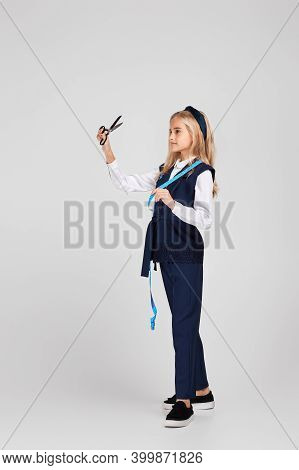 Little Girl Holding Tape Measure And Loooking At Scissors On Studio Background. The Child Dreams Of 