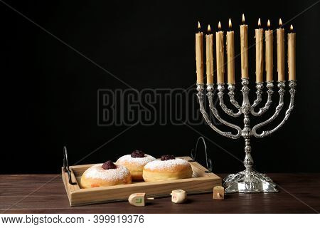 Silver Menorah Near Sufganiyot And Dreidels With Symbols Nun, He, Pe, Gimel On Black Background. Spa