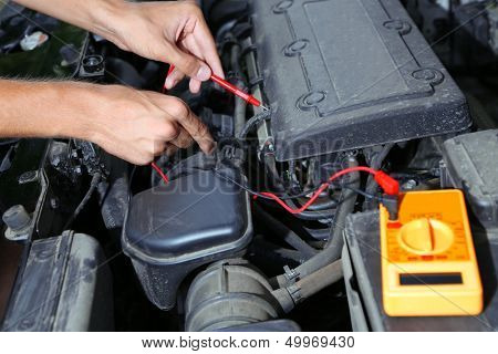 Auto mechanic uses multimeter voltmeter to check voltage level in car battery