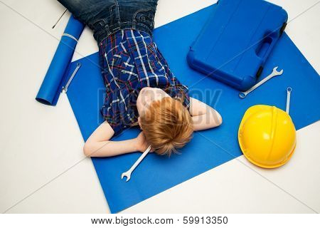 Funny little mechanic boy with wrench tools lying on a blueprint 