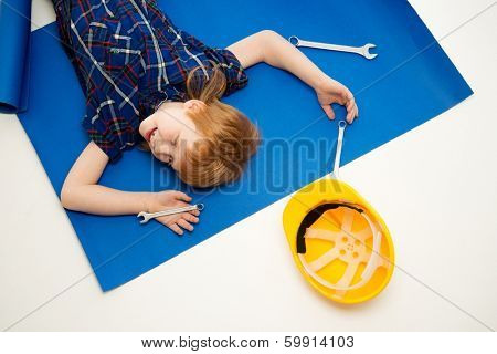 Funny little mechanic boy with wrench tools lying on a blueprint 