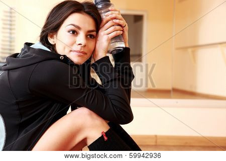 Young thoughtful fit woman resting and holding botter of water at gym