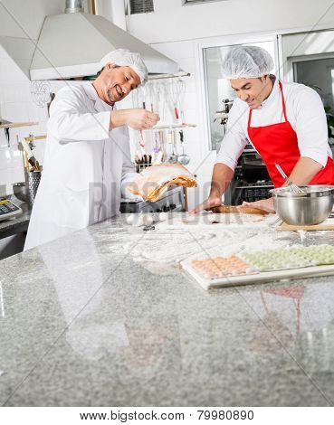 Smiling male chefs cooking ravioli pasta together at counter in commercial kitchen
