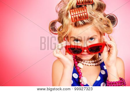 Fashionable little girl in her mother's hair curlers and pin-up sunglasses. Kid's fashion, cosmetics. Pin-up style.
