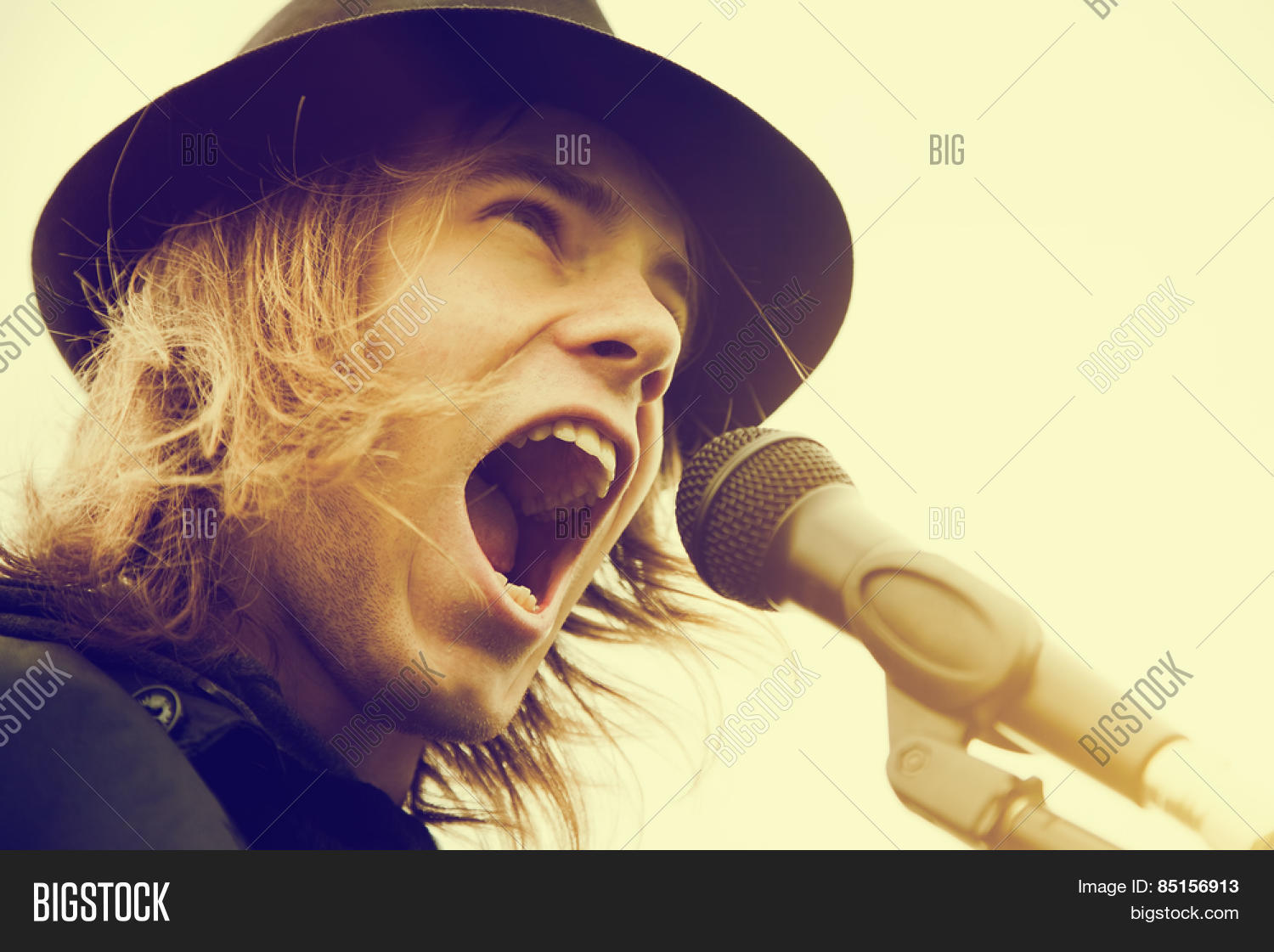 young man with long hair and hat singing, shouting to microphone
