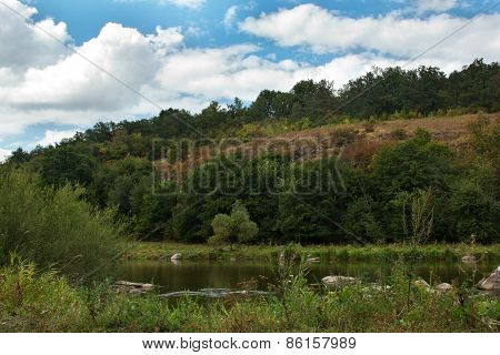 landscape of a green grassy hills, trees, river and sky