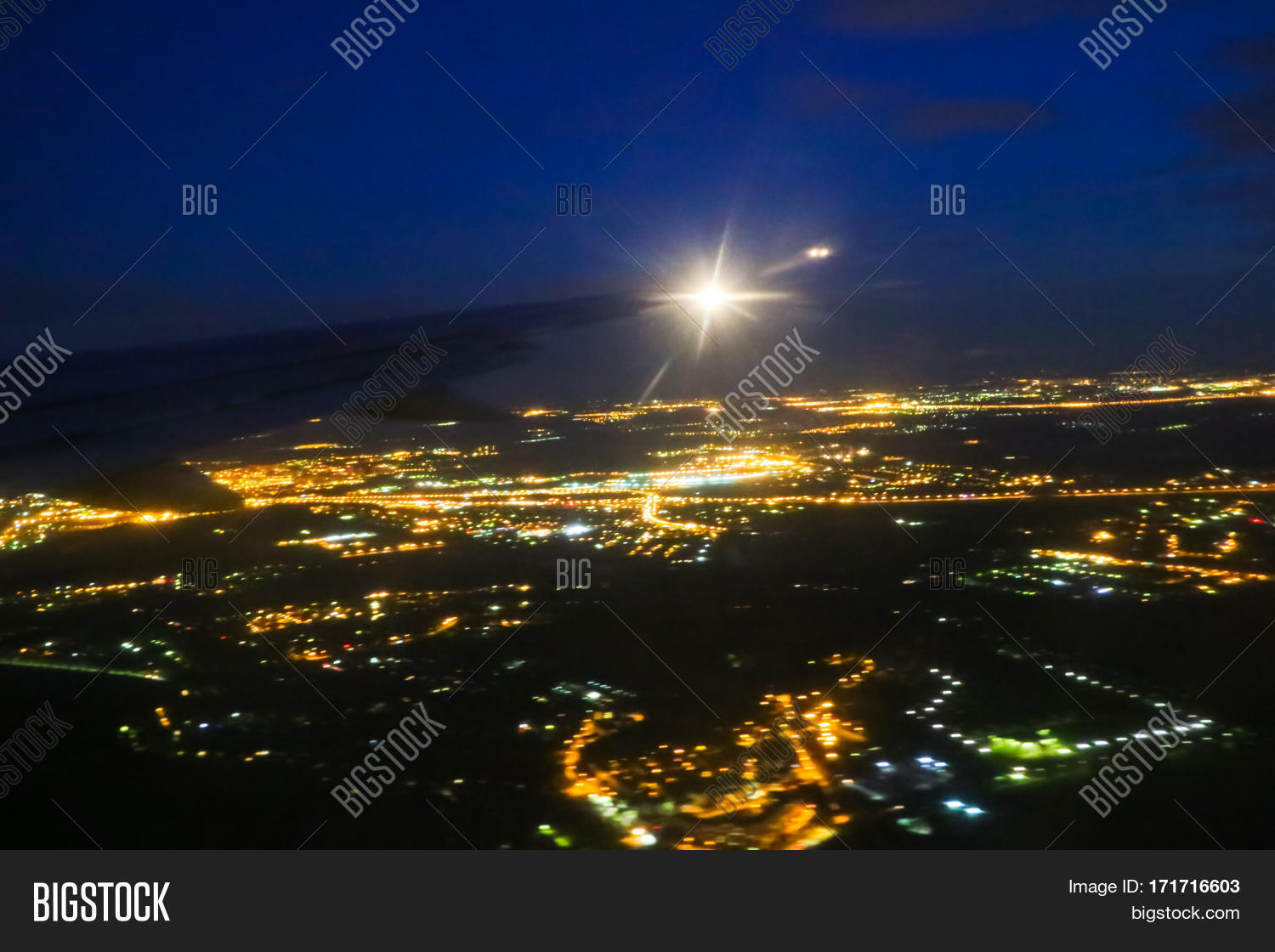 the wing of an airplane flying in the sky and nighe lights