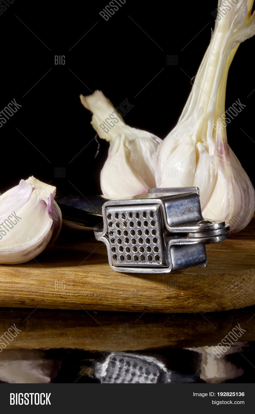 garlic press and cloves of garlic laid on a wooden table back
