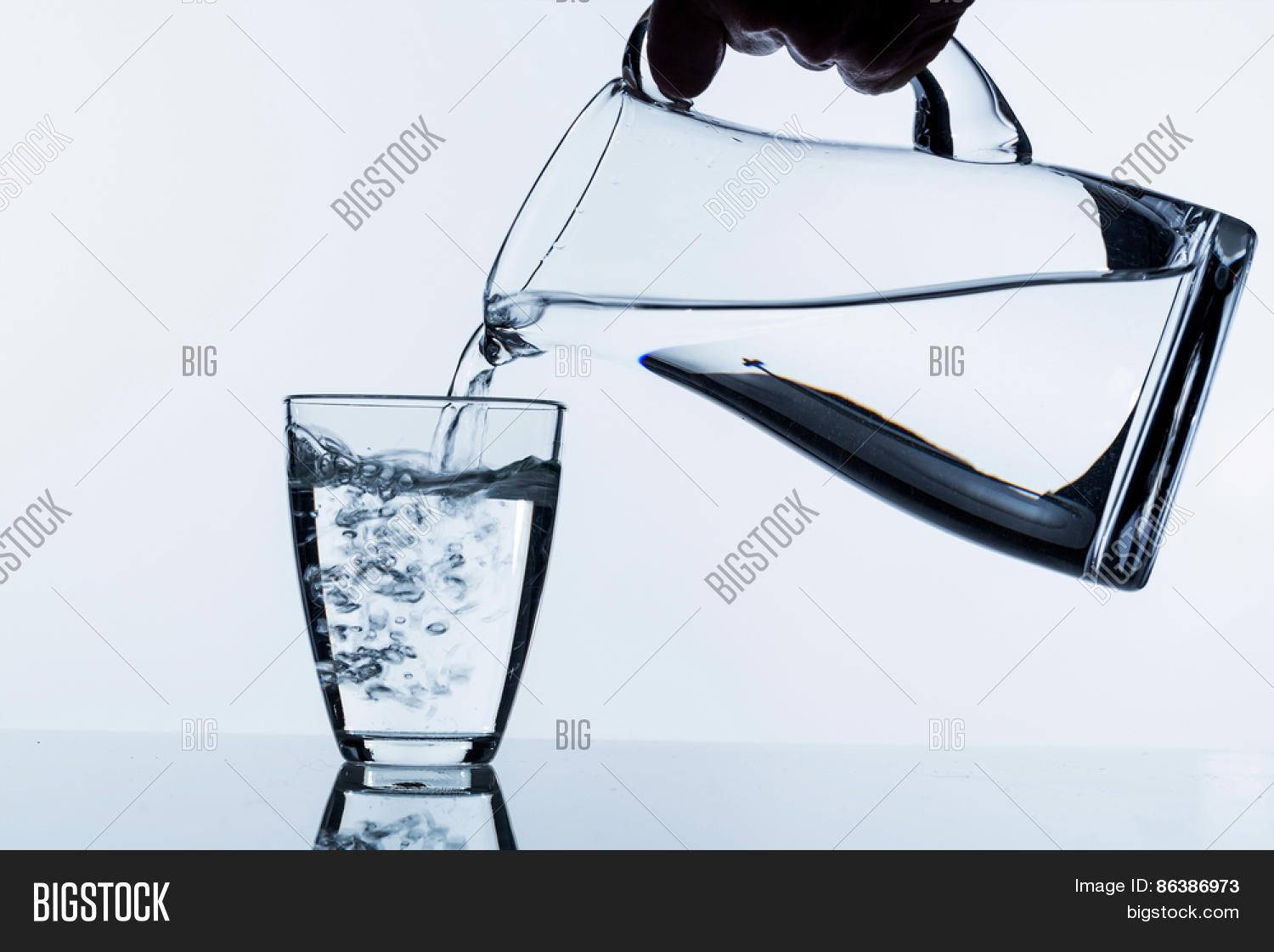 pure water is emptied into a glass of water from a jug.