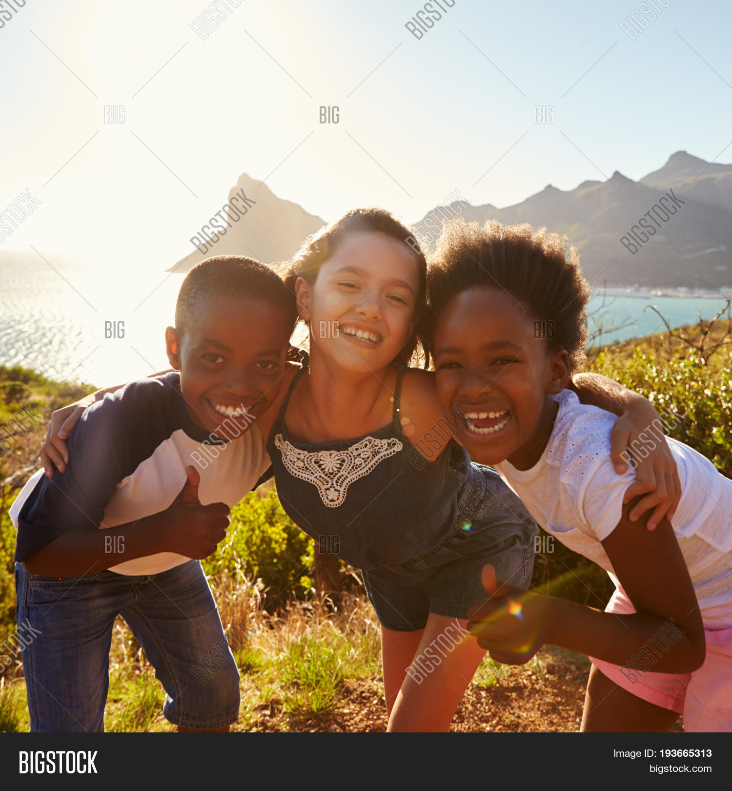 portrait of smiling children standing on cliffs by sea