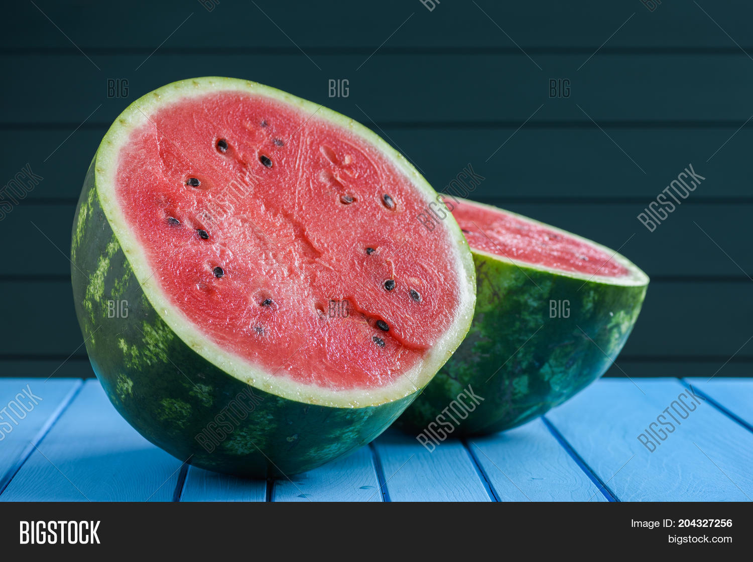 fresh raw watermelon with seeds cut in halves on blue background