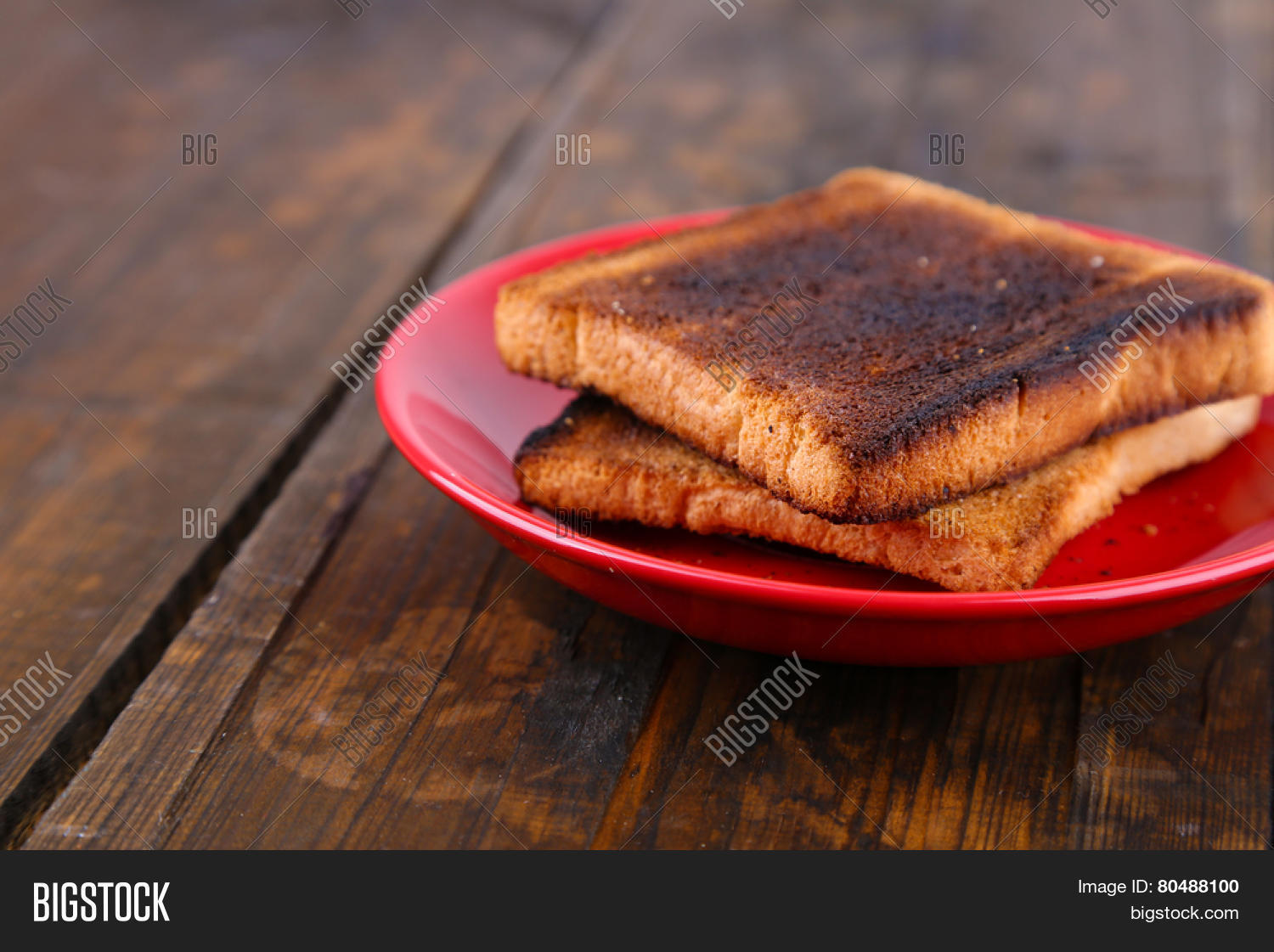burnt toast bread on red plate, on wooden table background