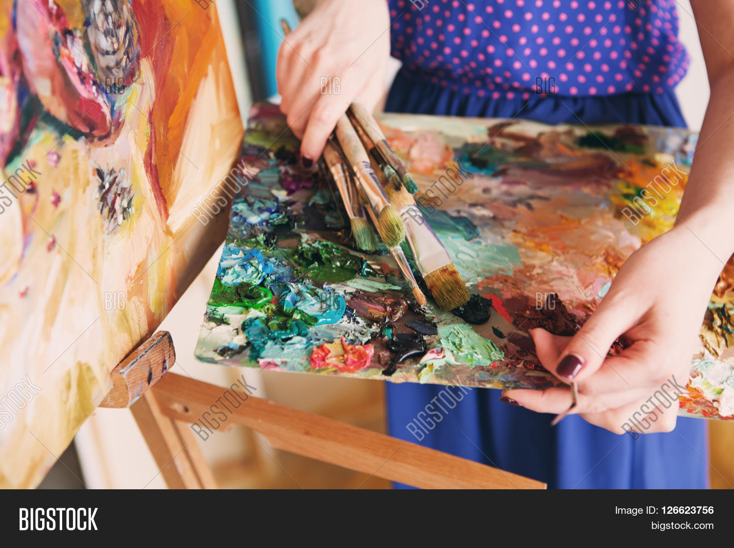 artist paints a picture of oil paint brush in hand with palette