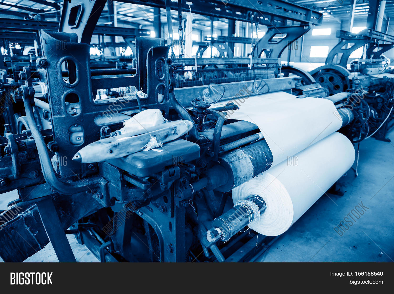 a row of textile looms weaving cotton yarn in a textile mill.