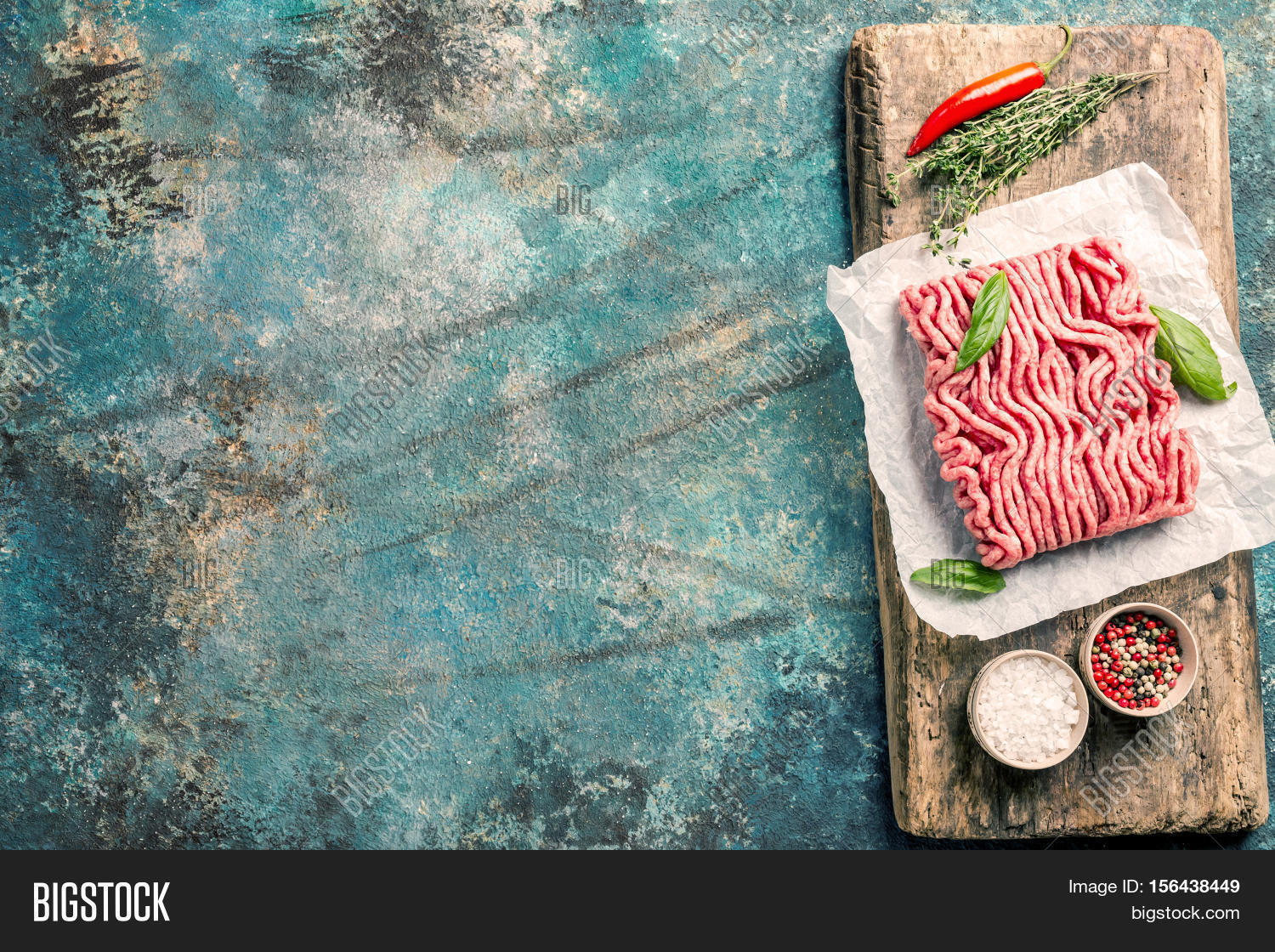 raw minced meat with olive oil and seasoning on paper over blue