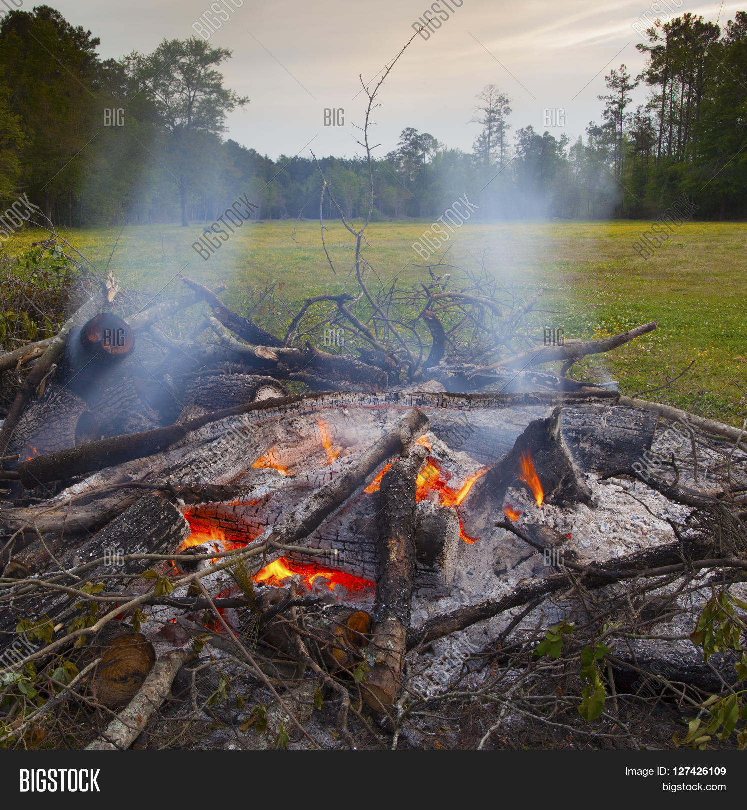 coals that are blazing hot in a burning brush pile on a field