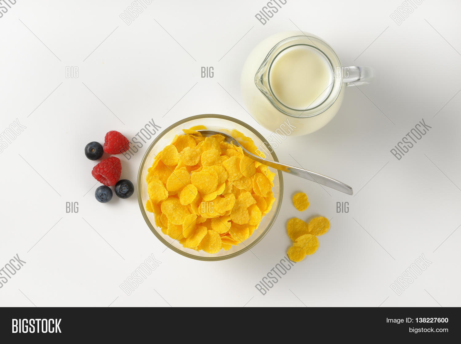 bowl of corn flakes and jug of milk on off-white background with