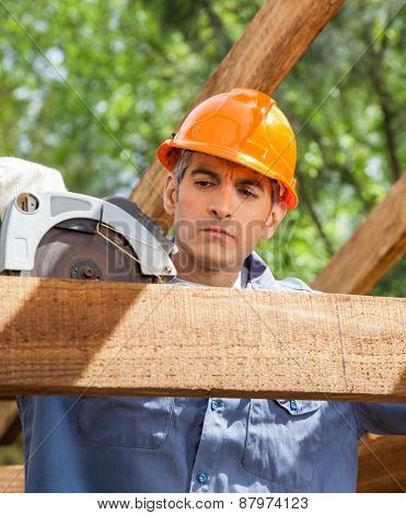 male construction worker using electric saw on timber frame at